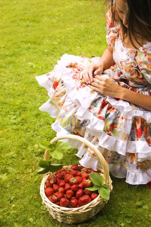 Young caucasian woman sitting near basket full of strawberries の写真素材