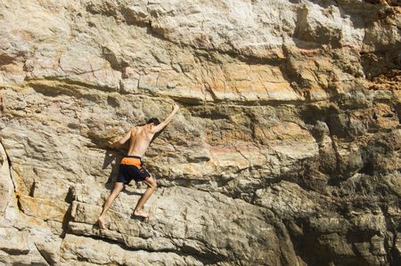 Young man climbing a cliff above seaの写真素材