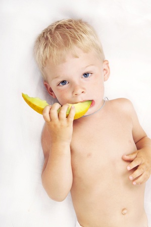 Adorable child of 3 years eating melon, on whiteの写真素材