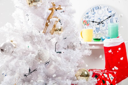 White christmas tree with golden decorations, clock on white table, presents near the tree, grey...