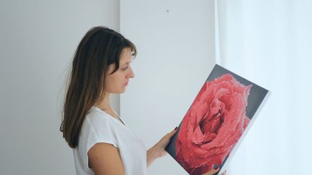 Long-haired girl hanging painting on wall at houseの写真素材