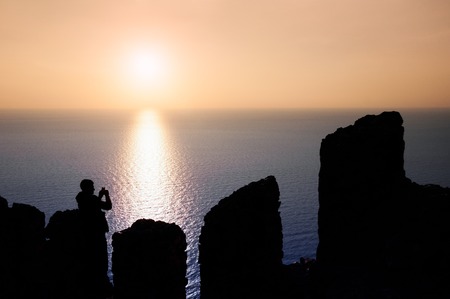 Man tourist taking photos of a sunset in the sea from the castle of Alanya in Turkey with mobile phoneの写真素材