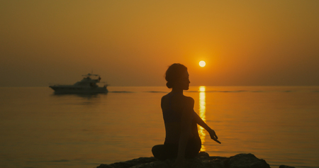 Girl practices yoga near the ocean during sunrise timeの写真素材