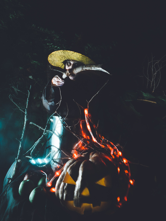 Wicked frightening witch hexing with cane above the cauldron in dark forest . Halloween Horror Scene