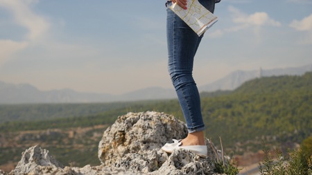 Closeup of female legs tourist travelling around the world with map, standing high above the green mountainsの写真素材