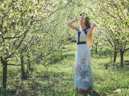 Young beautiful woman with long blond hair in bay leaf wreath dreaming with closed eyes in spring blossom cherry garden.の写真素材