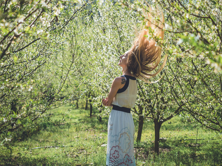 Young beautiful woman with flying long blond hair in bay leaf wreath in spring blossom cherry garden.の写真素材