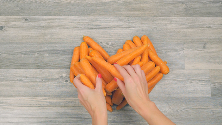 Closeup of womans hands put carrots in the shape of a heart on a white background. Healthy food conceptの写真素材