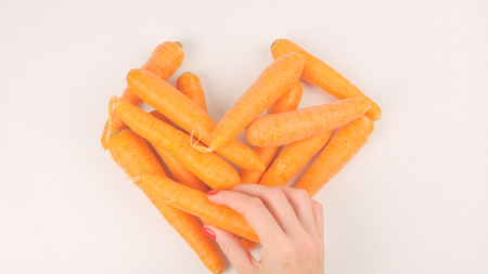 Closeup of womans hands put carrots in the shape of a heart on a white background. Healthy food conceptの写真素材