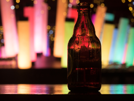 Dark glass beer bottle at the bar counter with colour changing decoration glowing flashing lamp cylinder column fluorescent neon on backgroundの写真素材