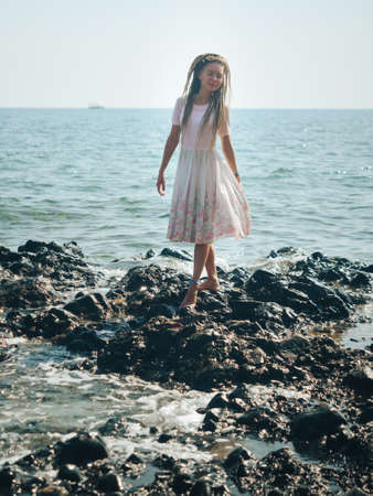Dreadlocks fashionable girl standing alone on the rocks by the seaの写真素材