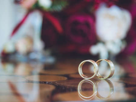 Closeup of wedding rings on the table of glass and wood. Bouquet in bokehの写真素材