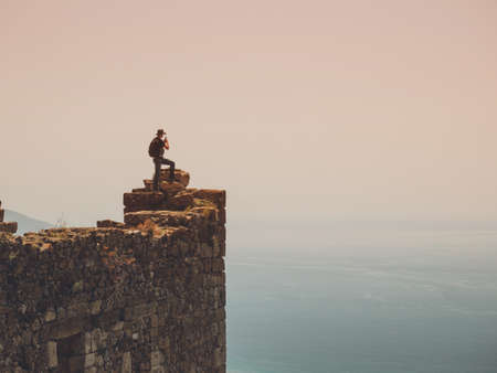 Traveler taking pictures of amazing landscape on smart phone while standing on a rock with beautiful sea viewの写真素材