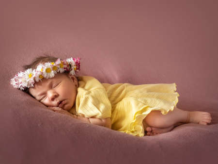 Adorable 8 days old newborn baby girl sleeping in daisy wreath yellow knitted dress on a soft plaid.