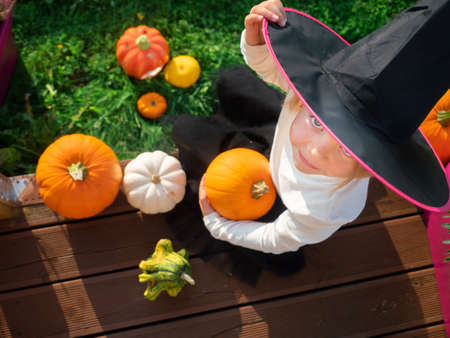 3 years old girl in witch costume sitting with pumpkins on wooden terrace.の写真素材