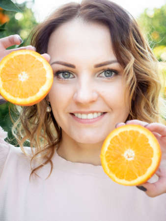 Portrait of young pretty woman holding two halves of oranges in front of her face