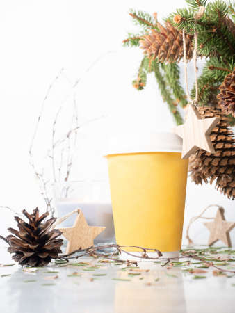 Take away cardboard cup on the table with christmas decor. Fir tree bouquet, candle and wooden star...