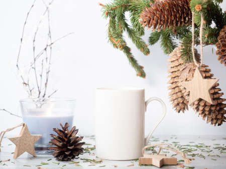 White ceramic mug on the table with christmas decor. Fir tree bouquet, candle and wooden star...
