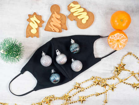 Black face mask decorated with christmas ornament. Flat lay of christmas decorations with protective...