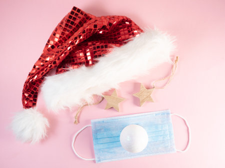 Medical face mask with christmas ornaments and red Santa hat on pink backgroundの写真素材
