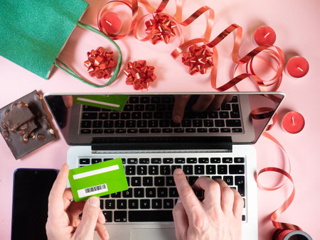 Top view of man making online shopping buying gifts with credit card. Gift, candles, chocolate, ribbons on pink backgroundの写真素材