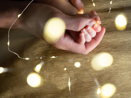 Closeup of father holding baby hand with christmas lights on golden backgroundの写真素材
