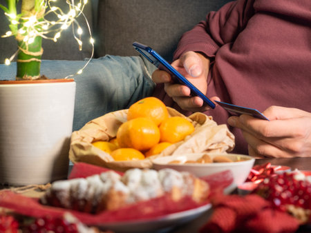 Closeup view of man with cellphone sitting in the living room near Christmas decorated tableの写真素材