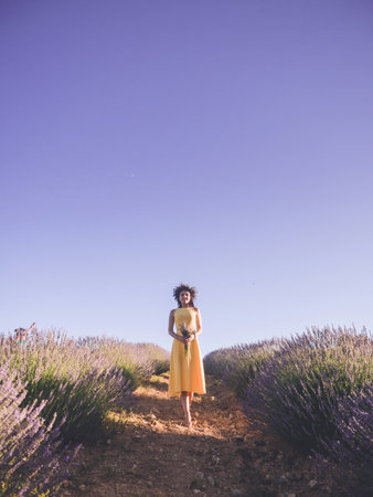 Carefree and happy young beautiful woman in yellow dress standing with bouquet in lavender field enjoying lifeの写真素材