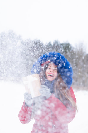 Woman in red coat holding present and enjoying snowfall. Beautiful snowy winterの写真素材