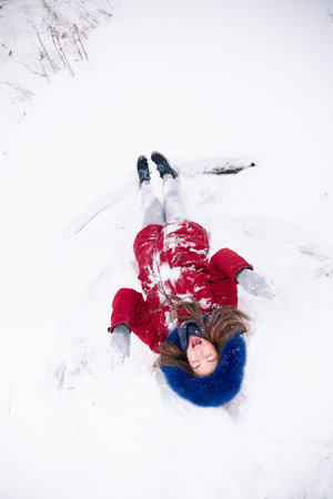 Young funny woman in red coat lying on the snow. Enjoying winter time