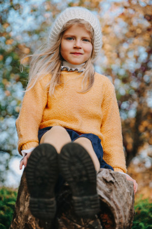 Adorable girl in yellow blouse and white beret sitting on the tree. Beautiful golden autumnの写真素材
