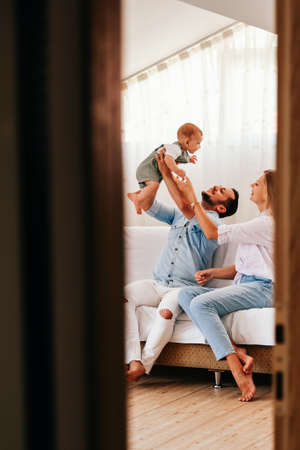 Young happy family. Careful young caucasian parents playing with their little cute baby boy in living roomの写真素材