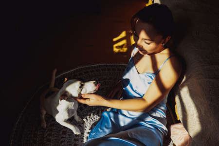 Beautiful brunette woman caress her dog jack russell terrier sitting on the floor near the bed. Morning happinessの写真素材
