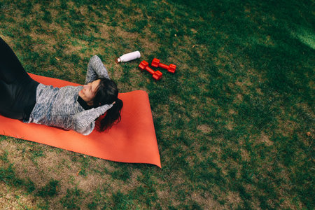 Young woman in sportive clothes doing crunches on mat to warm up. Exercising outdoors