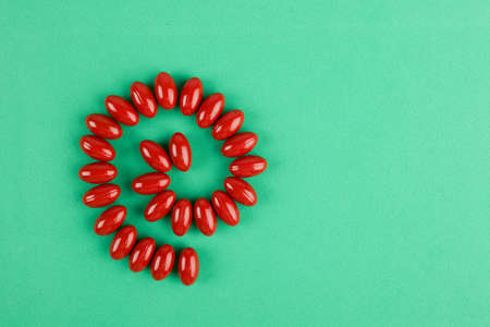 Red capsules put in abstract shape of intestine on green background. Pills, antibiotics, healthcare.
