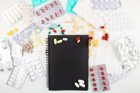 Flat lay of black notebook and variety of different pills on the table. Healthcare and Medicine