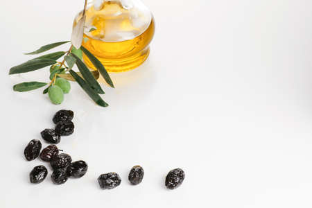 Extra virgin olive oil in a glass bottle isolated on white background. Smoked black olives in glass plate in front of bottleの写真素材