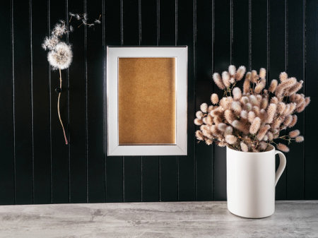 Empty wooden frame where you can write your text hanging on black wooden wall, dry flowers in cups...