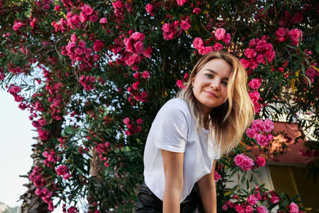 Portrait of young happy woman in white shirt with natural makeup in blooming bush and looking at cameraの写真素材