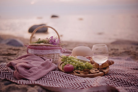 Beautiful summer picnic served for one person at sunset on beach with white wine, croissants, cookies, and fresh fruits.の写真素材