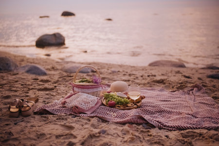 Beautiful summer picnic served for one person at sunset on beach with white wine, croissants, cookies, and fresh fruits.の写真素材