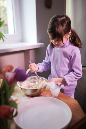 Little girl in violet clothes knead the dough in the kitchen. Preparing apple pie. Homemade food and...