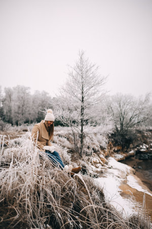Unrecognizable woman in warm ugg boots holding cup of tea enjoying winter frozen nature. Morning breakfast at nature. Travel, adventure concept, warm winter clothes.の写真素材