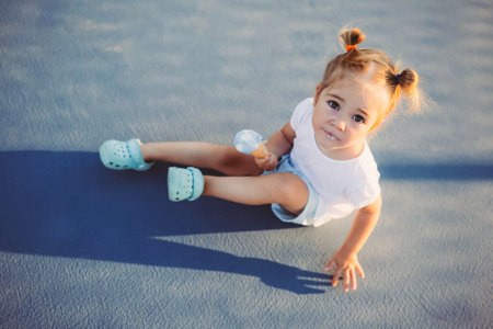 Adorable 2 years old girl eating ice cream outdoors, summer time. Conceptual active sweet kid...