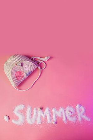 Summer text made of sand and girl straw handbag on pink background with copy space. Summer vacations with children conceptの写真素材
