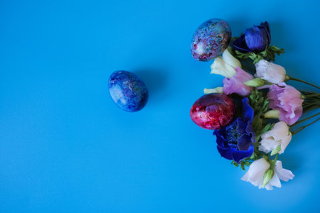 Beautiful bouquet of spring flowers and easter eggs on blue background. Top view with copy space....