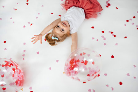 Adorable little girl lying on white background with balloons with heart shape papers inside it and around. Valentines Day conceptの写真素材
