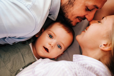 Young happy family. Adorable 6 month baby boy lying between his parents and looking curiously at cameraの写真素材