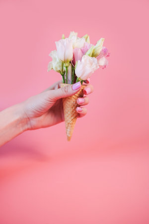 Close-up shot of a woman hand holds waffle cone with pink and white flowers on pink backgroundの写真素材