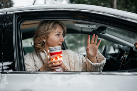 Attractive happy young woman hiding behind the cup of tea looking out the car window. Winter travel. Weekend recreationの写真素材
